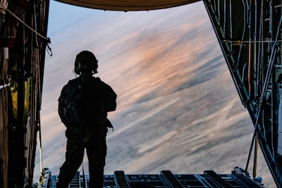 An loadmaster observes a jettisoned load of supplies from the rear of an aircraft in flight.