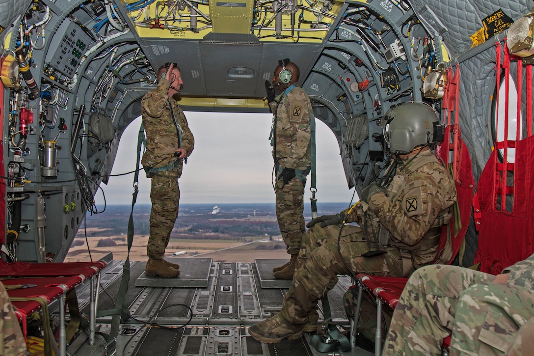 Two soldiers raise standing and facing each other raise one hand each aboard a helicopter.