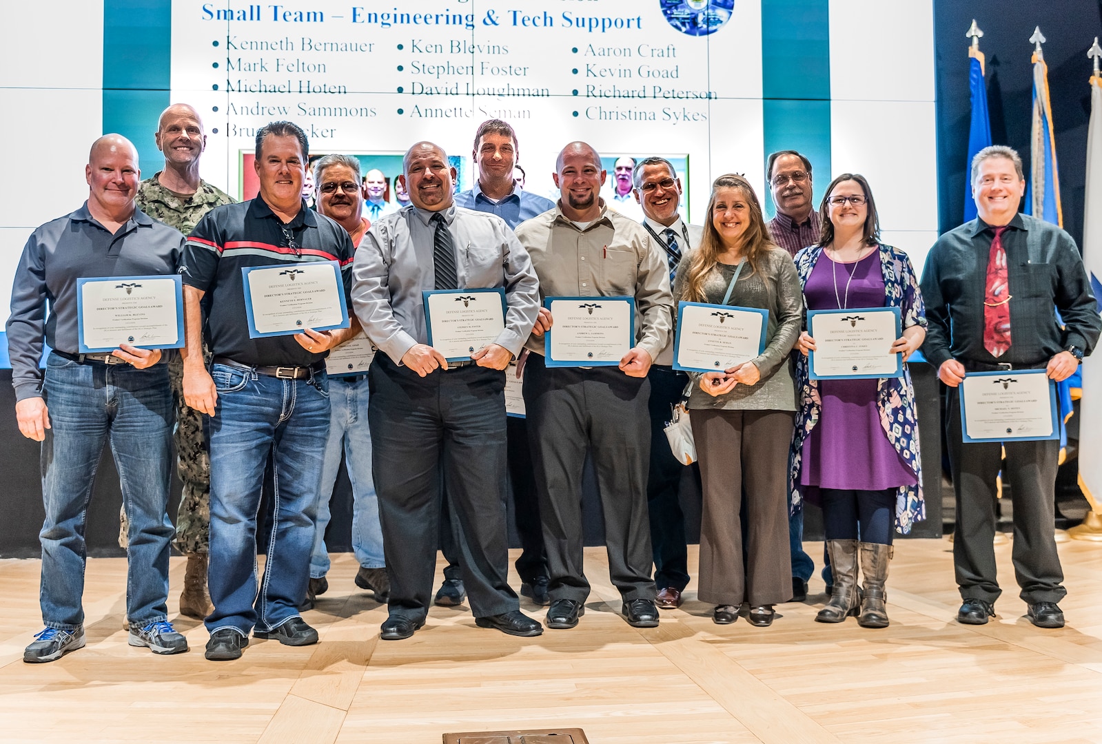 A group of associates stand on stage with certificates for a photo