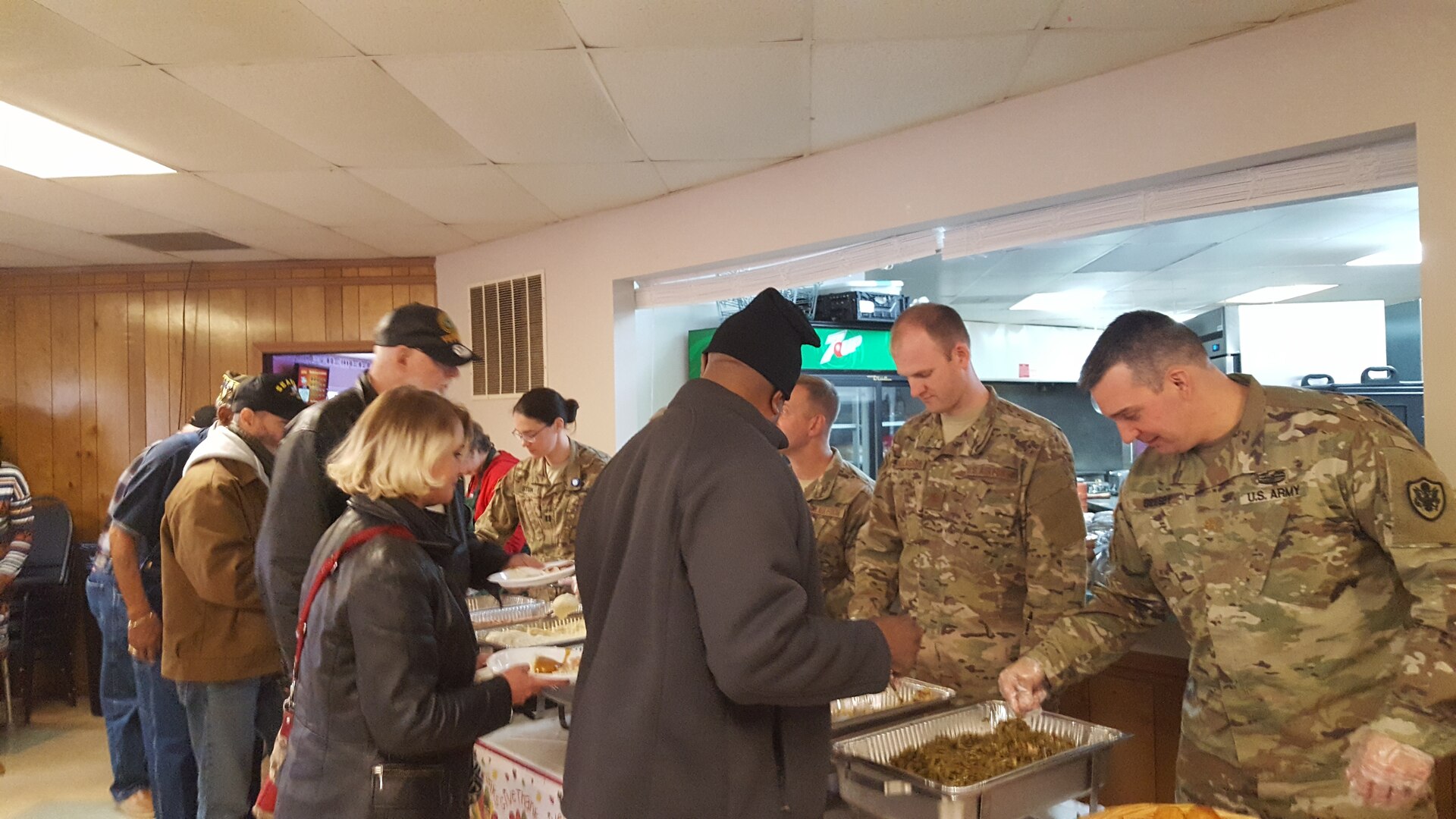 Members of the military serve Thanksgiving dinner to veterans as they walk down the buffet line