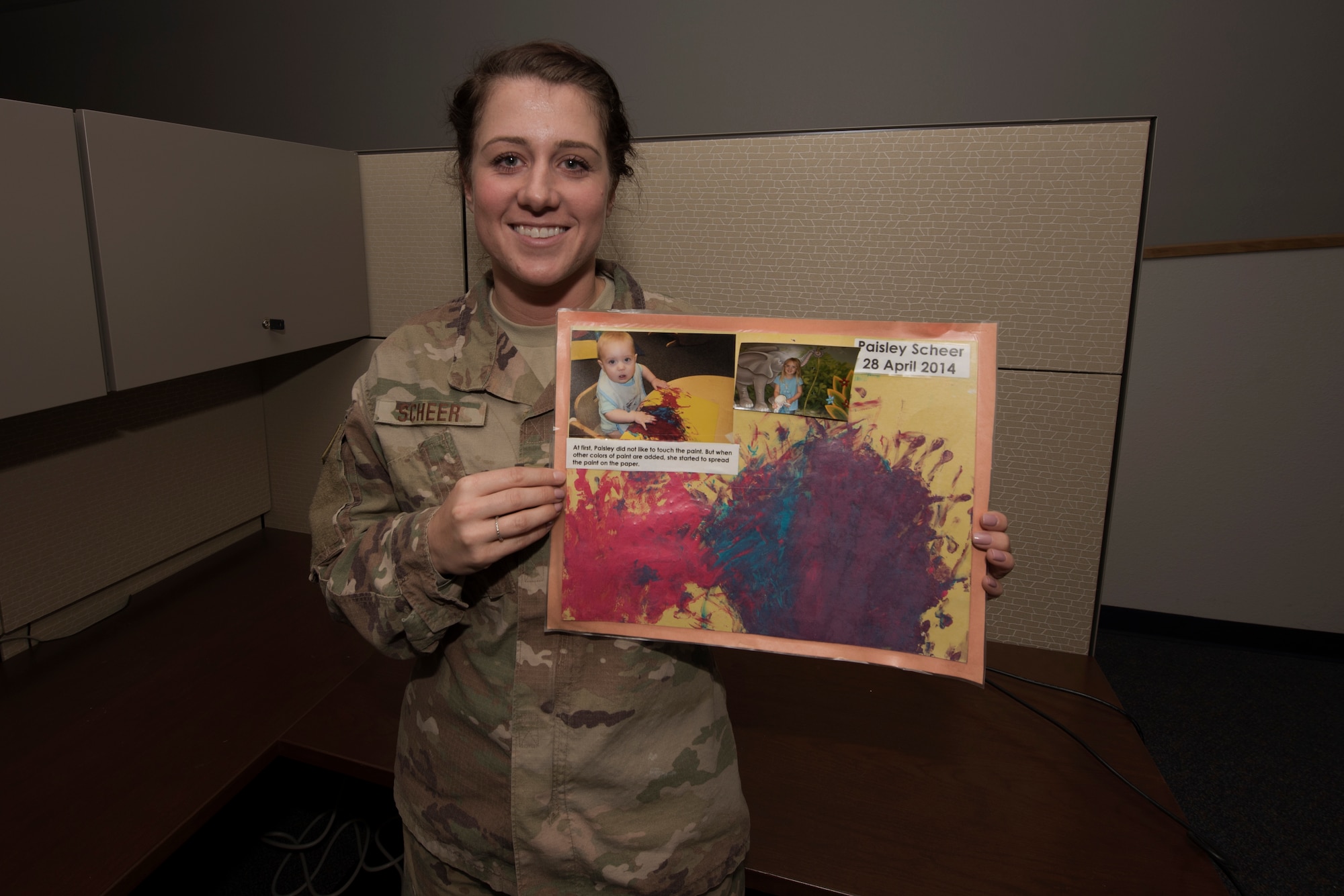 U.S. Air Force Staff Sgt. Amanda Scheer, 60th Contracting Squadron contracting specialist, poses for a photo in her office at Travis Air Force Base, California, while holding an original artwork her daughter Paisley created, Nov. 10, 2018. Scheer is a single mother and has served in the Air Force for six years. (U.S. Air Force photo by Tech. Sgt. James Hodgman)