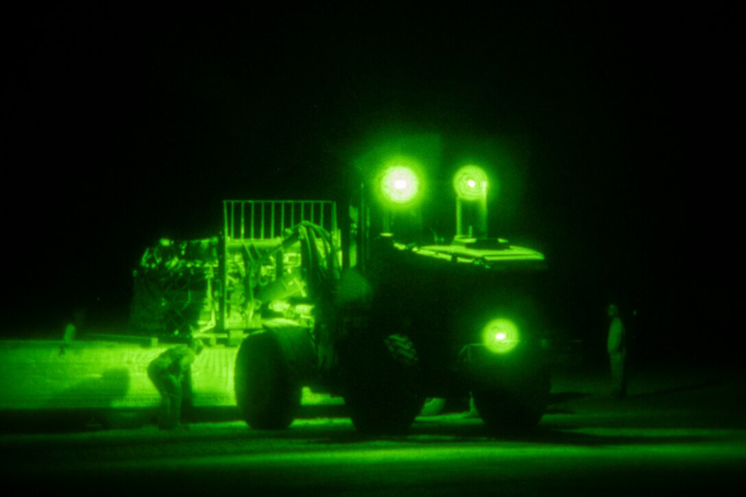 People gather around a military vehicle on a flightline, shown through a night-vision lens.