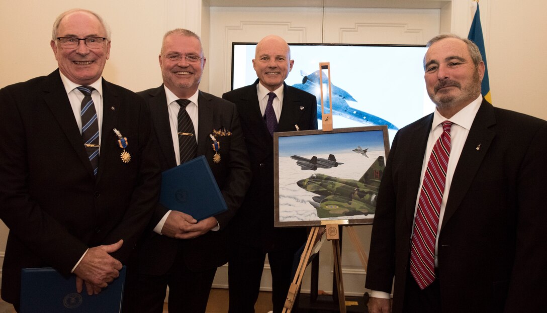From left to right, Col. Lars-Erik Blad, Maj. Roger Moller, Maj. Krister Sjober, and Retired U.S. Air Force Lt. Col. Tom Veltri stand beside the official photo which depicts the event that earned the Swedish pilots their U.S. Air Medals in Stockholm, Sweden, Nov. 28, 2018. The Swedish Airmen risked their lives to save an SR-71 and the aircrew, Tom Veltri and Duane Noll, on June 29, 1987. (U.S. Air Force Photo by Senior Airman Kelly O'Connor)