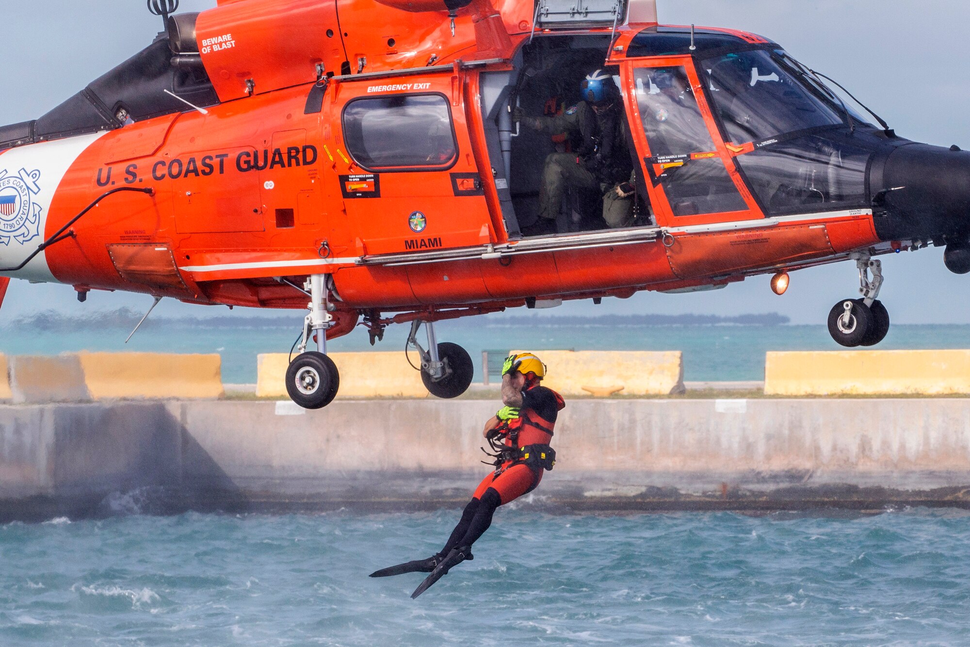 A U.S. Coast Guard rescue swimmer assigned to Air Station Miami jumps out of a, MH-65D Dolphin helicopter to simulate assisting an Airman with the 514th Air Mobility Wing during water survival training at Naval Air Station Key West's Truman Harbor, Key West, Florida, Nov. 16, 2018.