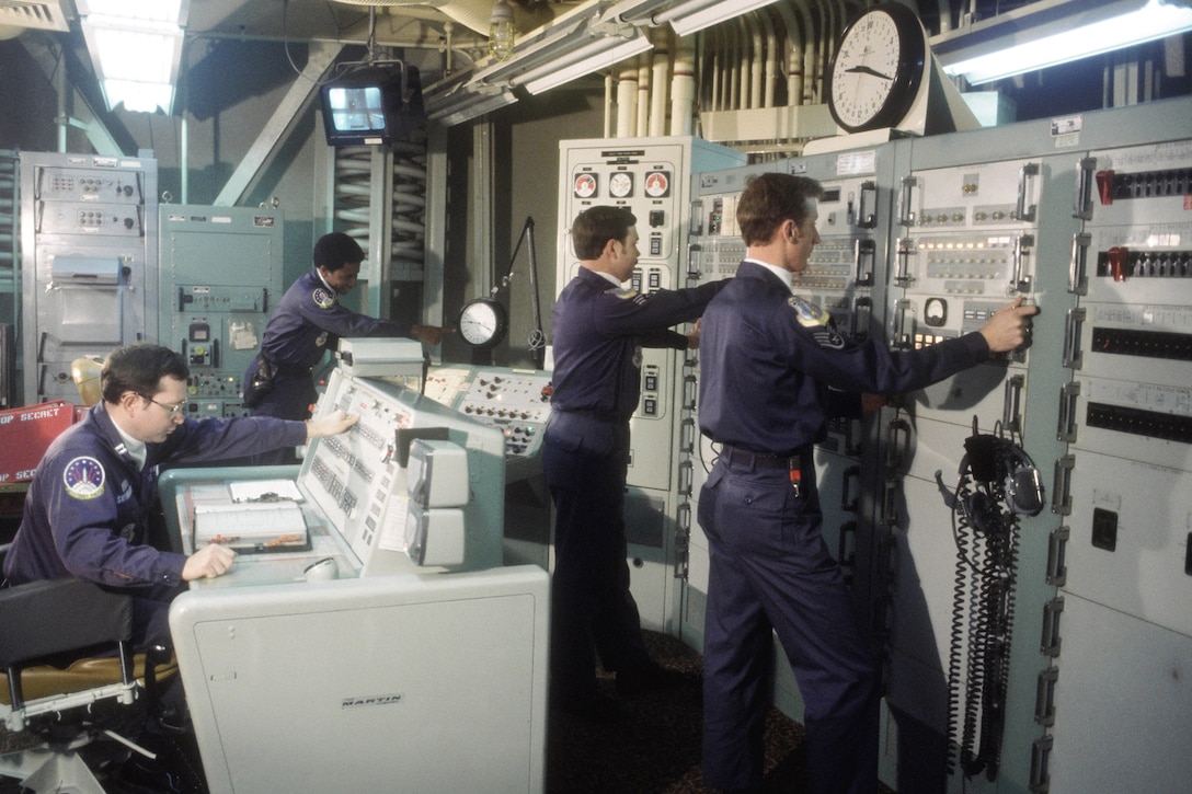Missile crew members push buttons on Cold War-era equipment.