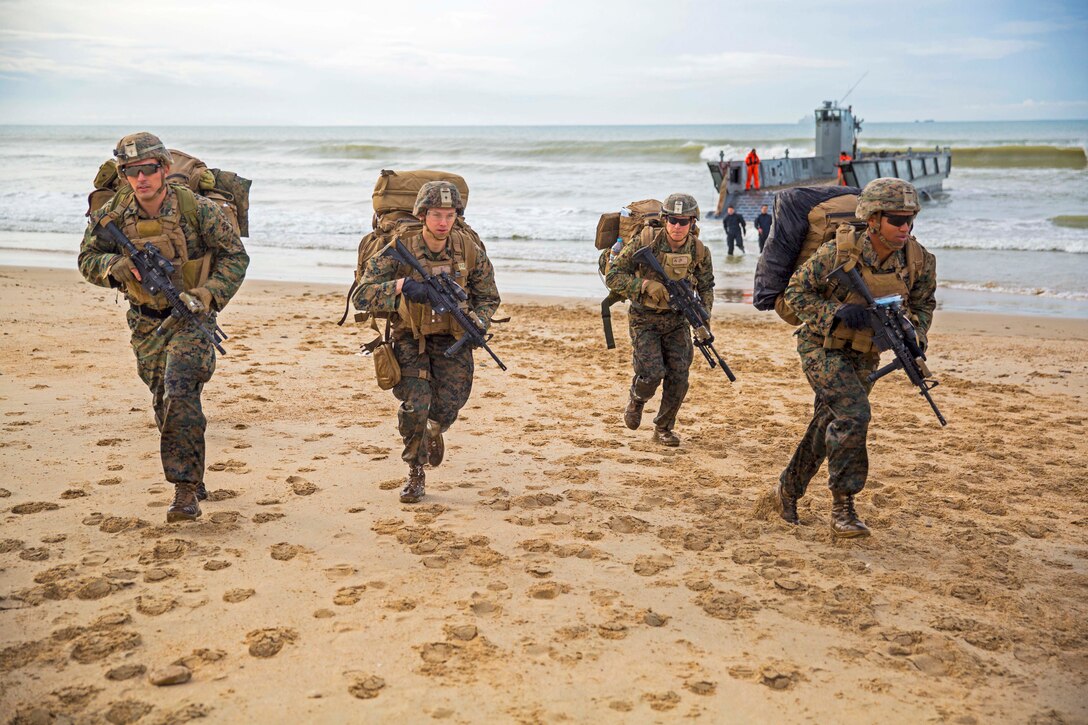 Four Marines race across the sand after landing on a beach.