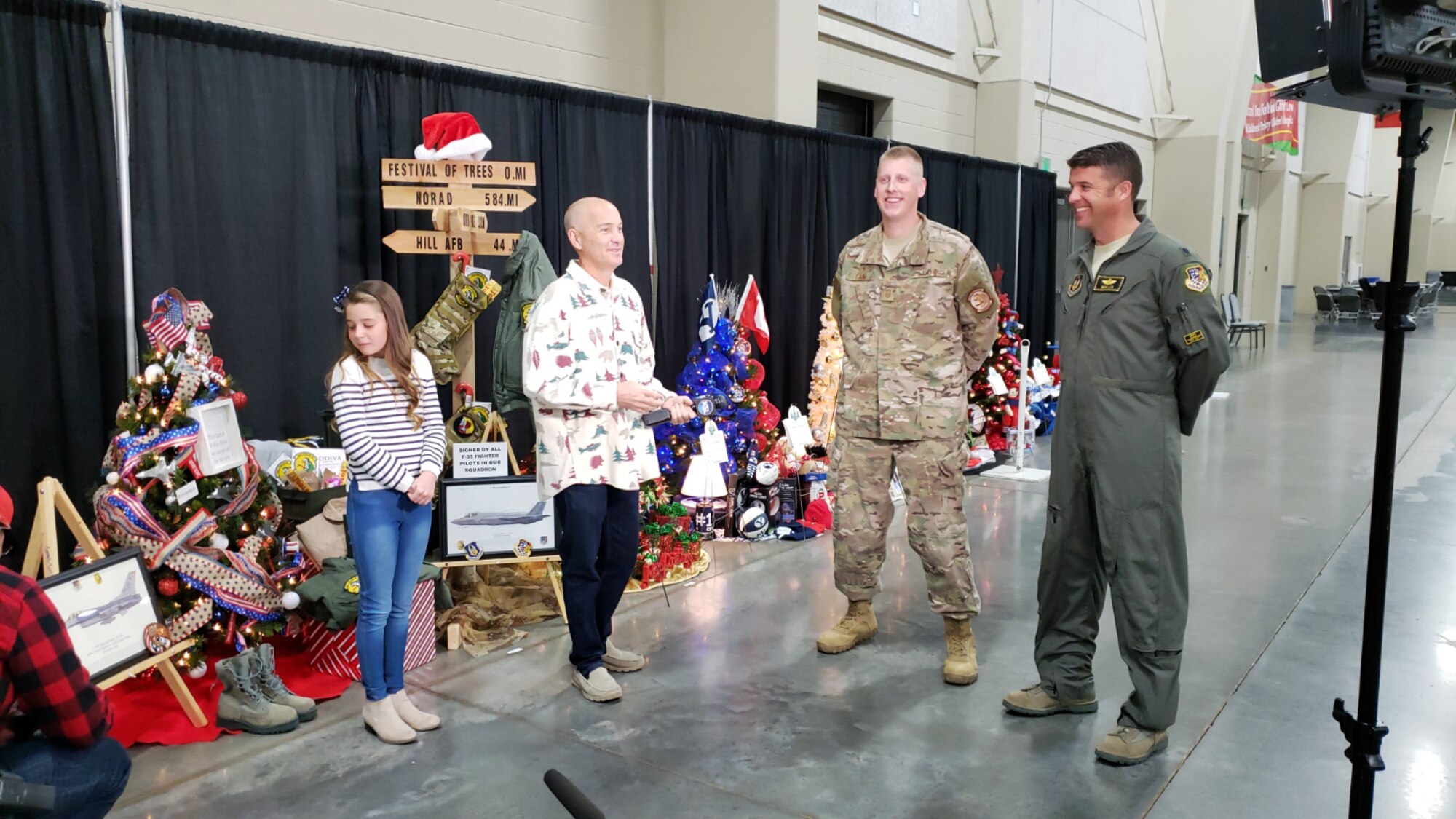 A local TV reporter interviews Senior Master Sgt. Christopher Cain and Lt. Col. Nathan Litz during the Festival of Trees event Nov. 28 in Sandy, Utah, along with Litz’s daughter, Gracie