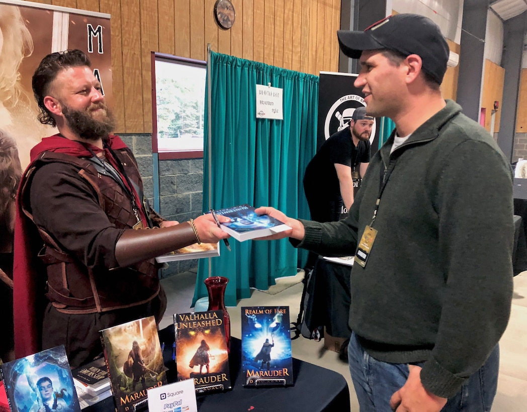 Former Marine LCpl. David Roach, author of the "Marauder" Viking fantasy series, hands his new book, "Runebinder" to Navy Lt. Rosert Pfeiffer, Office Naval Intelligence, Washington, D.C., at Vikings Con in LaPlata, Maryland, Oct. 20, 2018.