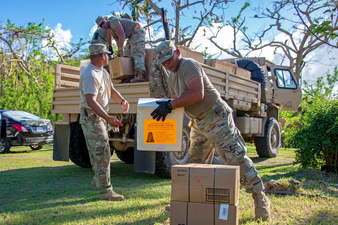 Several service members unload boxes of supplies from a truck.