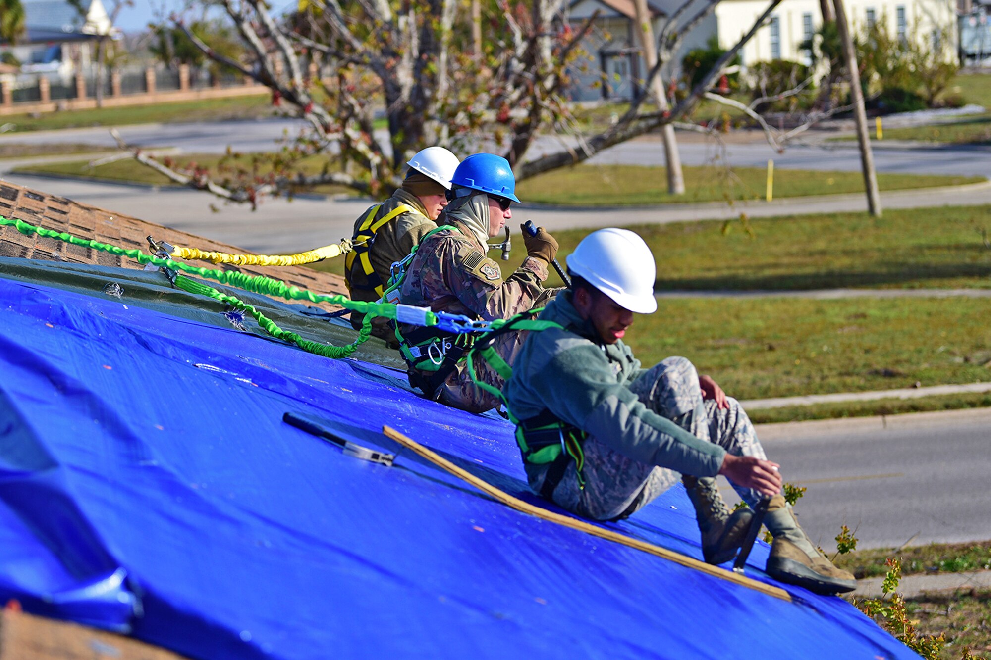 Three airmen sit on a roof while doing repairs.