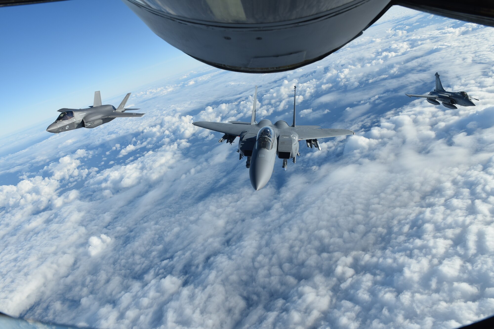 A Royal Air Force F-35 Lightning II, U.S. Air Force F-15E Strike Eagle, and French air force Dassault Rafale fly behind a U.S. Air Force KC-135 Stratotanker