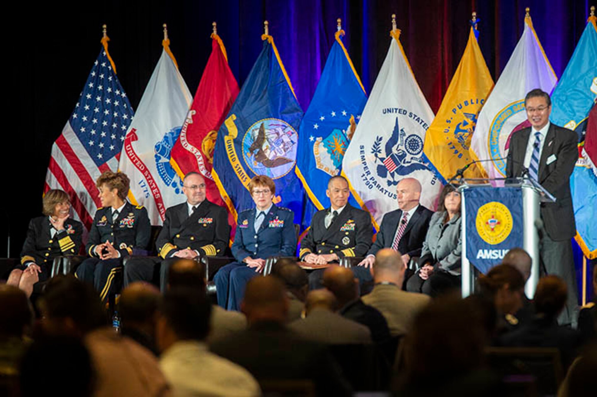 Dr. John Cho (far right), AMSUS executive director, introduces speakers (from left) Navy Vice Adm. Raquel Bono, Defense Health Agency director; Lt. Gen. Nadja West, Army Surgeon General; Vice Adm. Forrest Faison III, Navy Surgeon General; Lt. Gen. Dorothy Hogg, Air Force Surgeon General; Navy Rear Adm. Colin Chinn, Joint Staff surgeon, Dr. Richard Thomas, president of Uniformed Services University of the Health Sciences; and Dr. Terry Adirim, Deputy Assistant Secretary of Defense for Health Services Policy and Oversight. (MHS photo by Hannah Wagner)