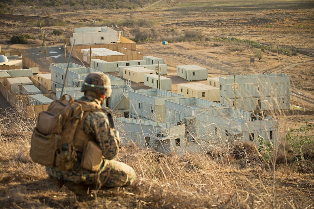 A Marine crouches uphill from a mock town.