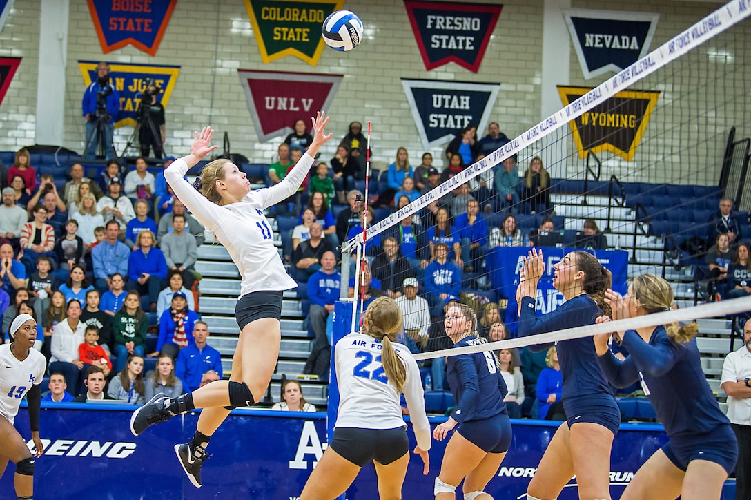 A volleyball player jumps in the air during a game while others look on.