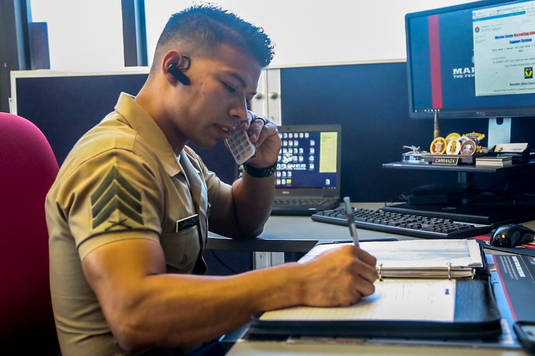 A Marine talks on the phone while sitting at a desk.