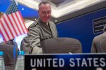 Marine Corps Gen. Joe Dunford smiles while preparing to sit at a table, with a mini American flag and a "United States" placard.