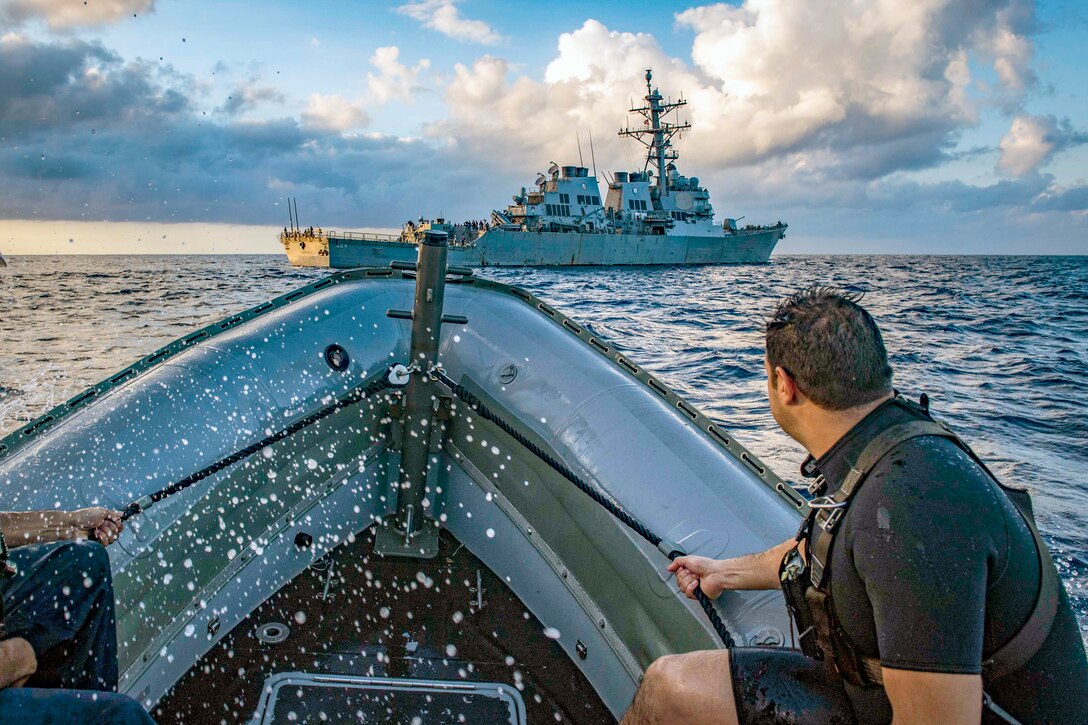 A sailor directs a boat next to a larger ship.