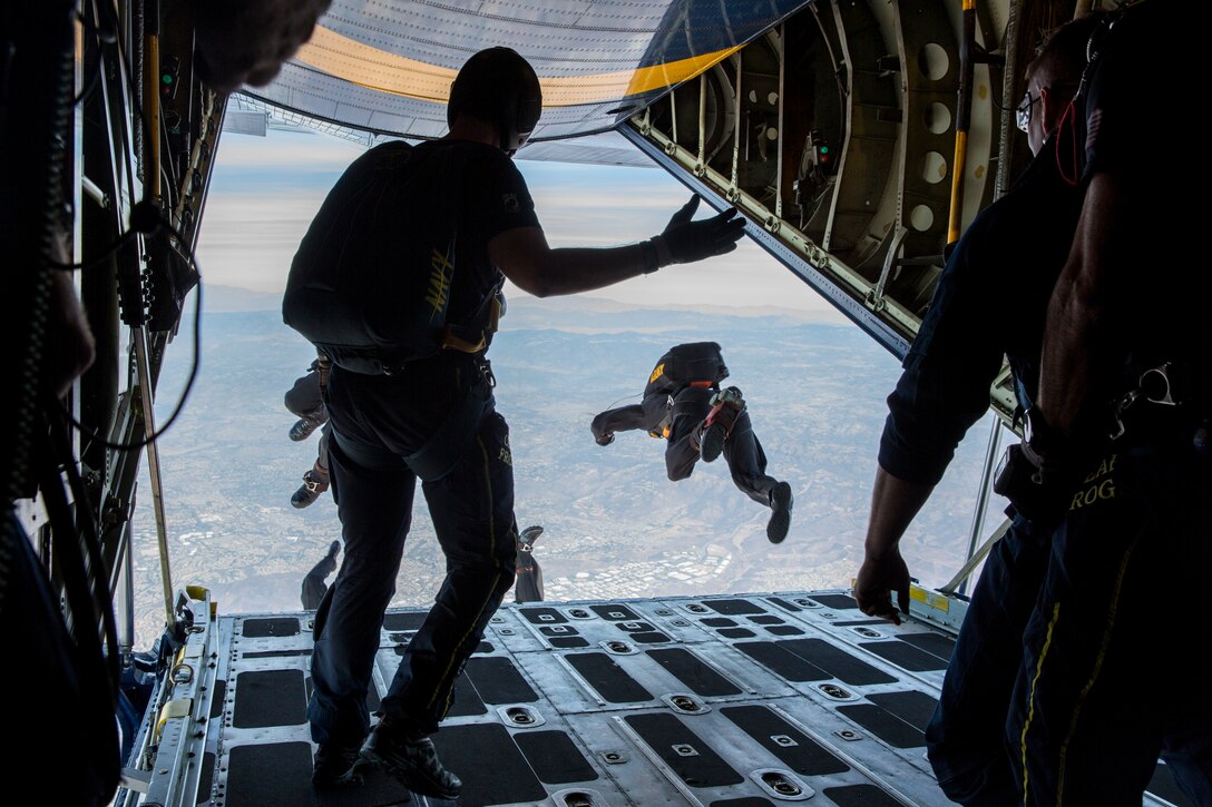 Service members  jump out of the back of an airplane.