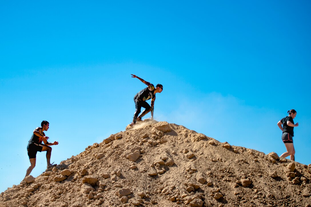 Three airmen traverse a dirt mound obstacle.