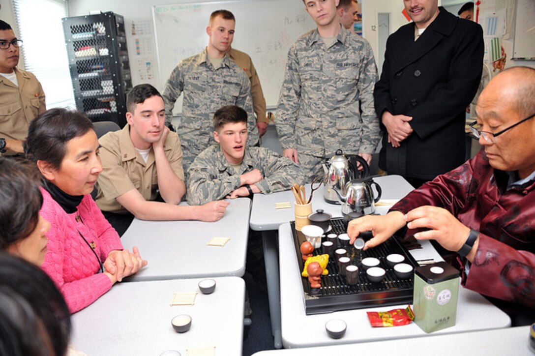 People sit around a table watching an instructor demonstrate a tea-tasking ceremony.