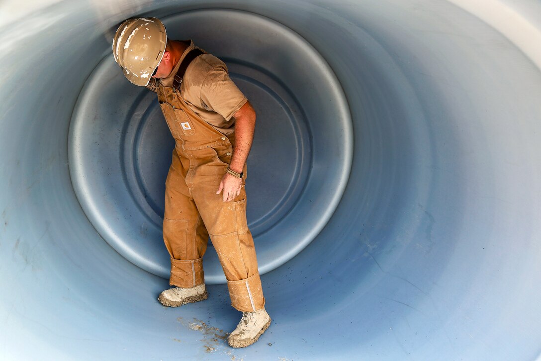 A sailor stands inside a large plumbing fixture.