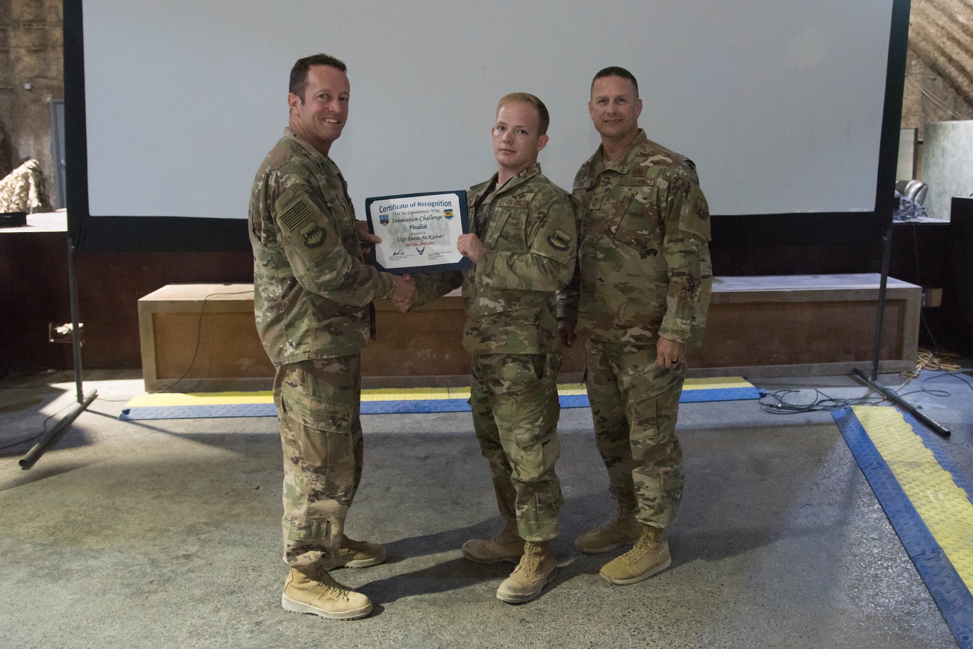 Brig. Gen. David Iverson, 332nd Air Expeditionary Wing commander, and Chief Master Sgt. Jason Tiek, 332nd AEW command chief, present the Red Tails Commander’s Innovation Challenge runner-up certificate to Staff Sgt. Devin McKeever, 332nd Expeditionary Maintenance Squadron fuel systems craftsman, Sept. 28, 2018, at an undisclosed location in Southwest Asia.