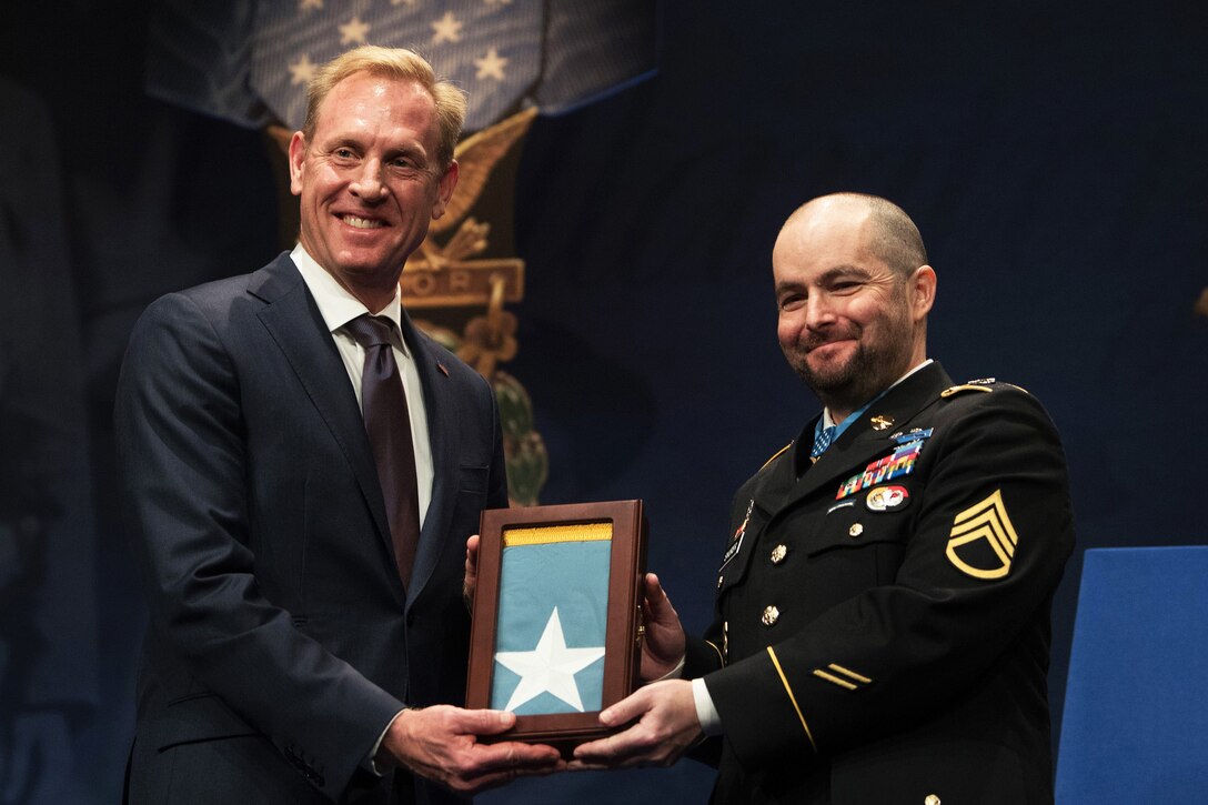 Deputy Defense Secretary Patrick M. Shanahan and an Army veteran jointly hold a framed flag and smile for a photo.