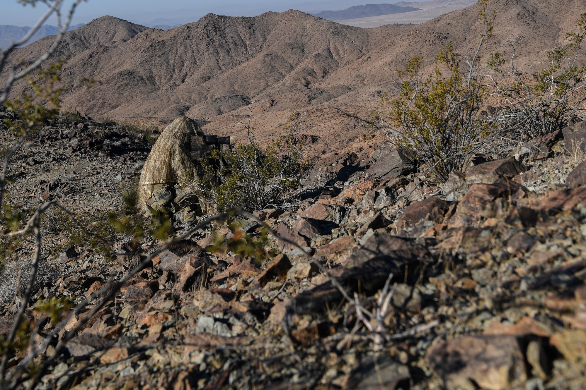 A Special Tactics operator with the 21st Special Tactics Squadron from Pope Army Airfield, Fort Bragg, North Carolina, observes enemy locations and movement through a scope during a scenario as part of NTC 18-10 at Fort Irwin, California, Sept. 1, 2018.