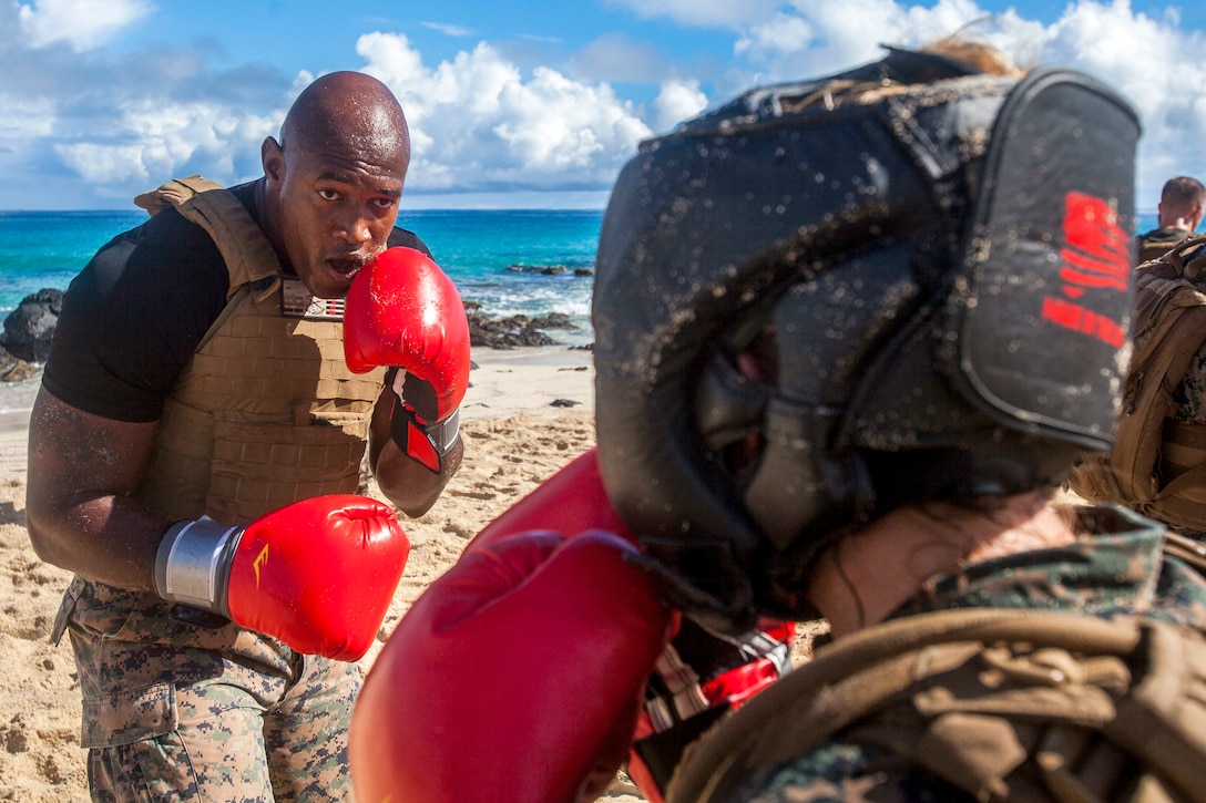 A Marine with red boxing gloves spars on a beach.