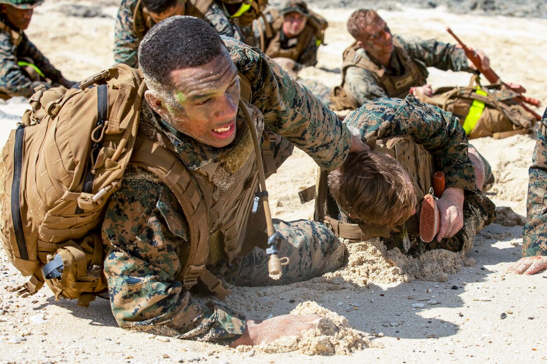 A Marine drags another Marine on a beach.