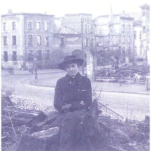A historic photo of a woman sitting in rubble.