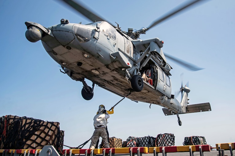 A helicopter hovers over the flight deck of a ship.