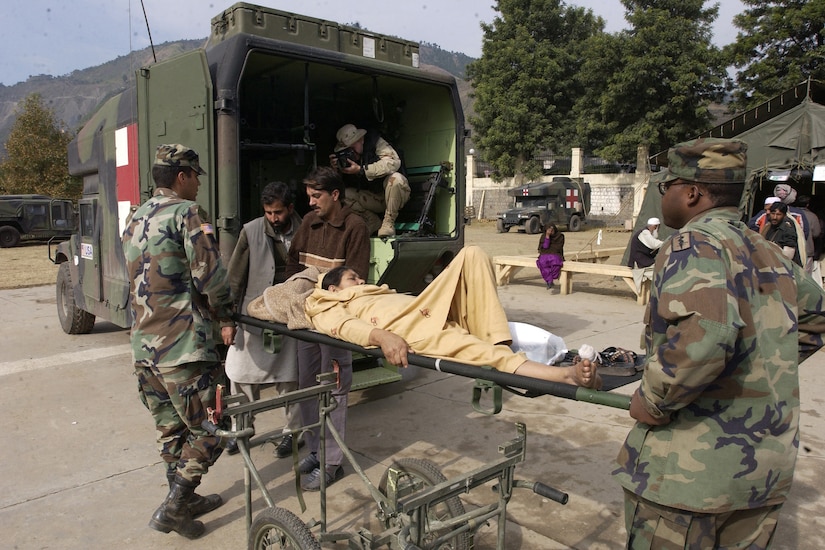 Soldiers hold a woman on a stretcher outside an ambulance.