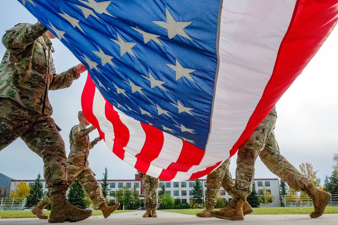 Soldiers fold a large flag in a field.