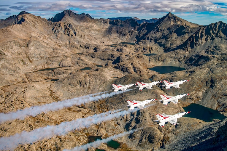 Airplanes fly in formation above mountains.