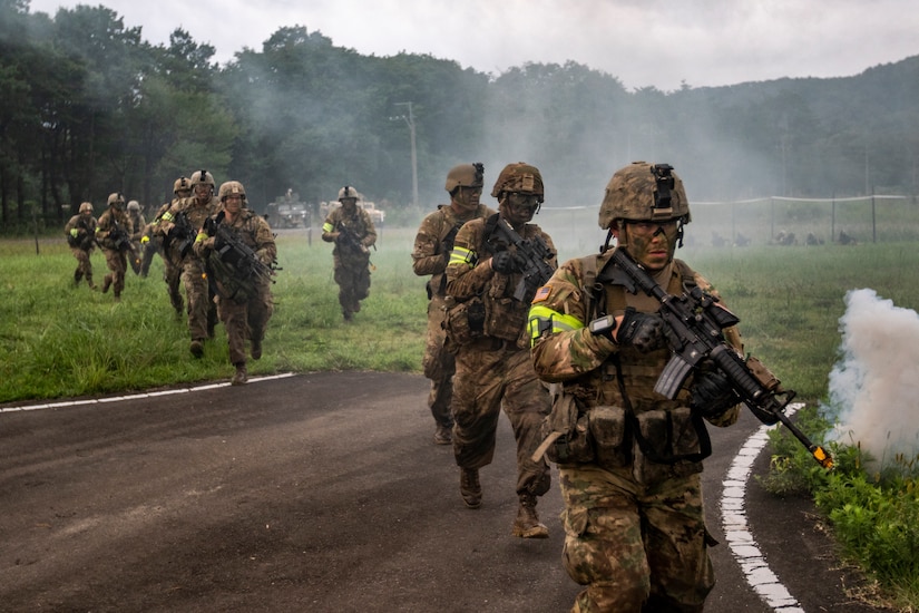 Soldiers in battle gear cross a road.