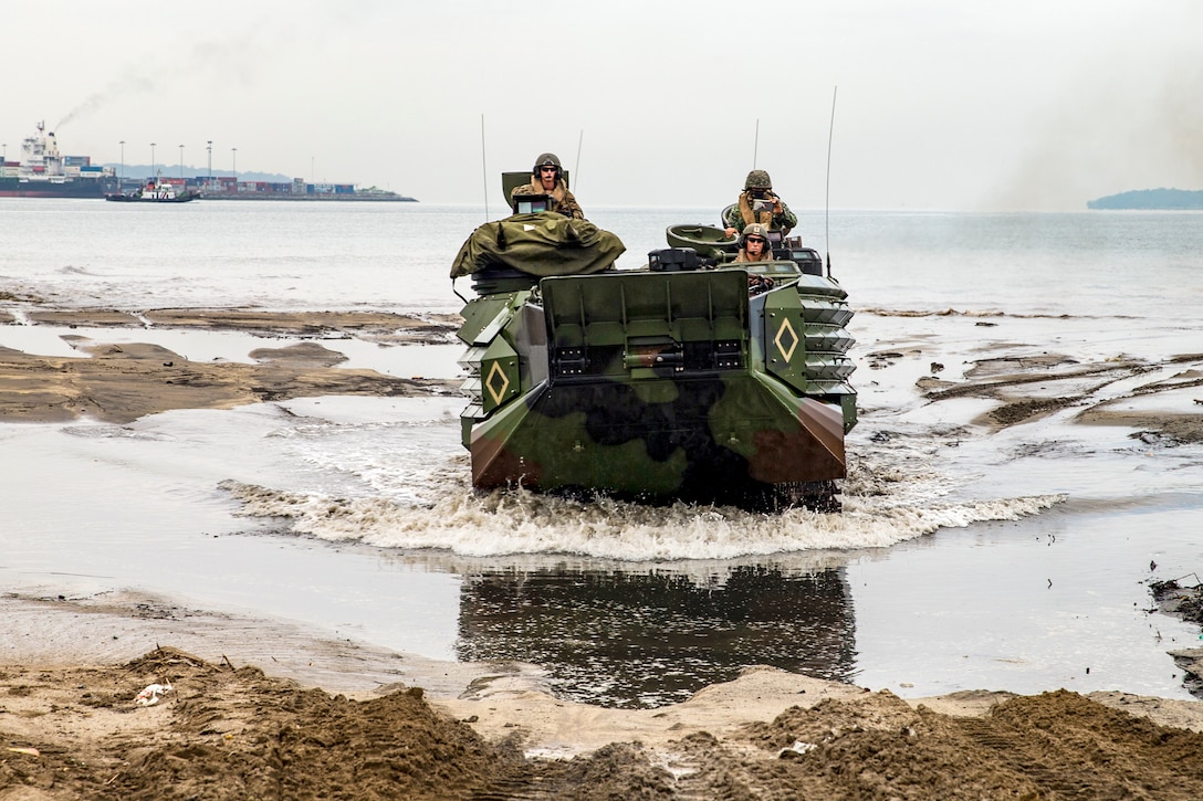 Marines drive on a beach in an amphibious vehicle.