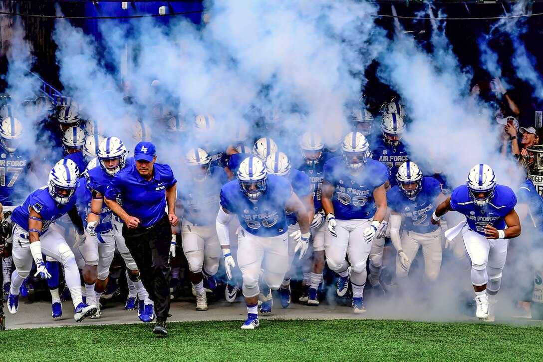 A football team runs through haze onto a field.