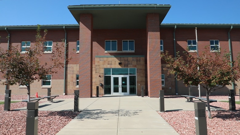 Picture of a brick building. A cement promenade leads to a magnificent doorway. There is also a big clear blue sky.