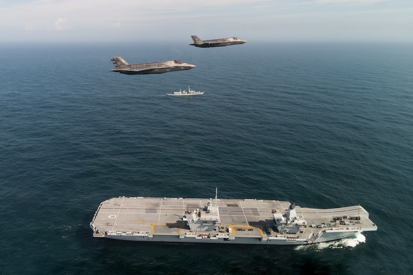 Two F-35s flies over a military ship.