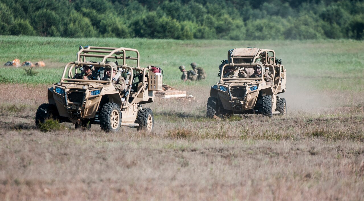 Two off-road vehicles drive in a field.