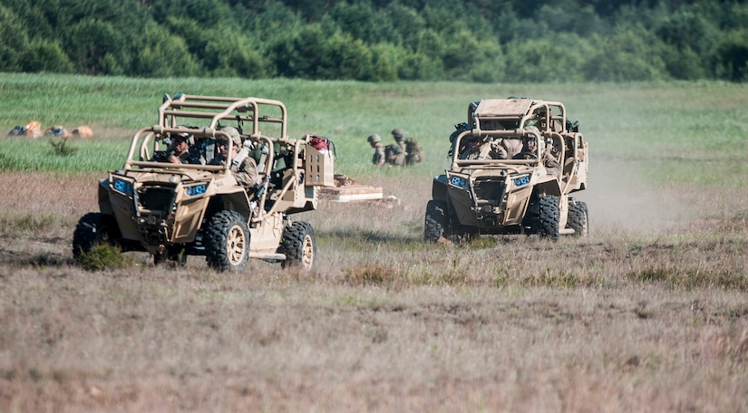 Two off-road vehicles drive in a field.