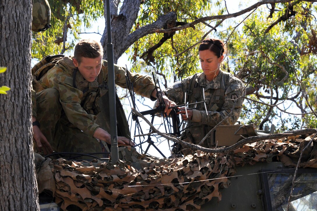 A male soldier and a female soldier set up an antenna in a tree.