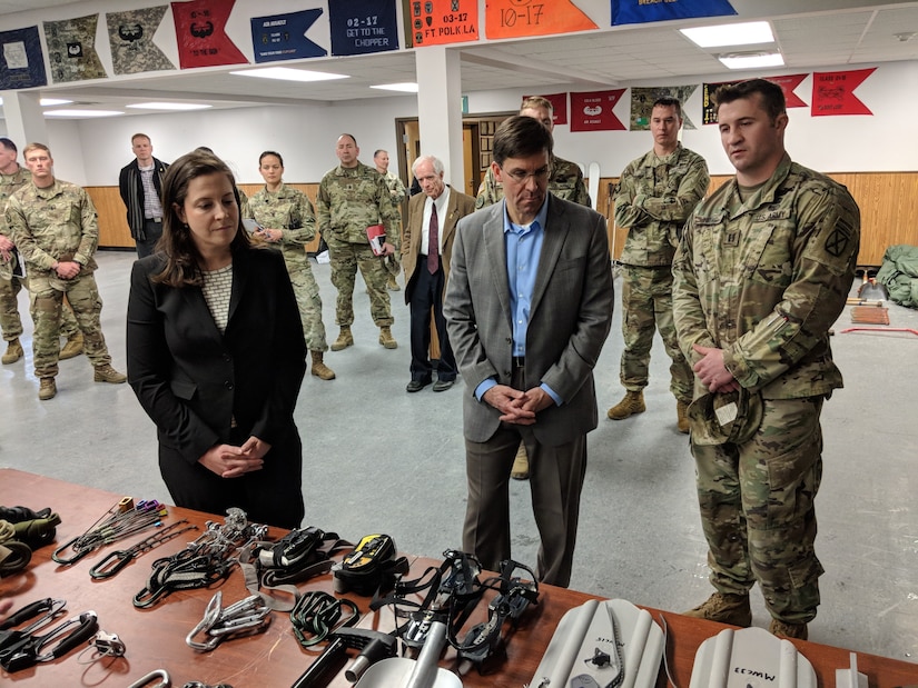 Army Secretary Mark T. Esper looks at items on a table in a room with service members and other officials.