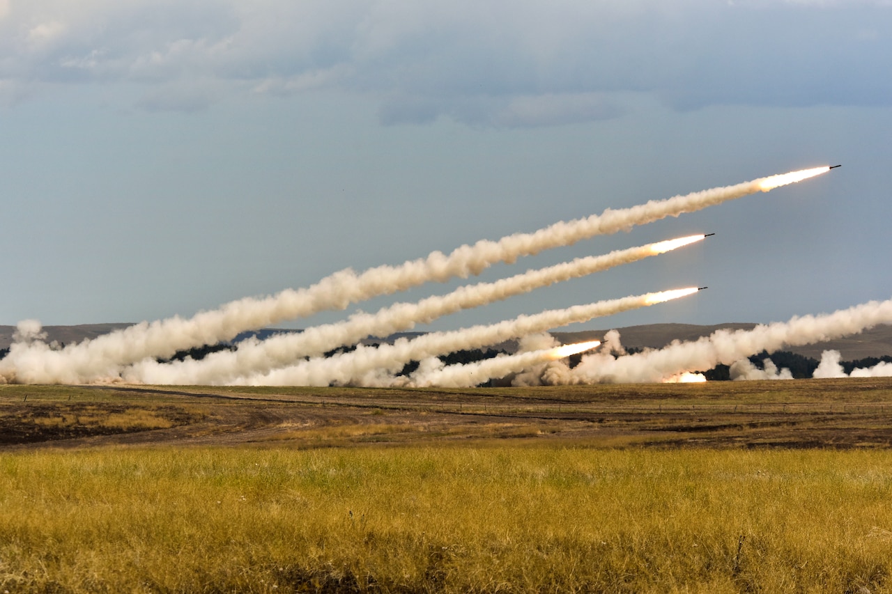 Several rockets shoot across a field, creating smoke trails.