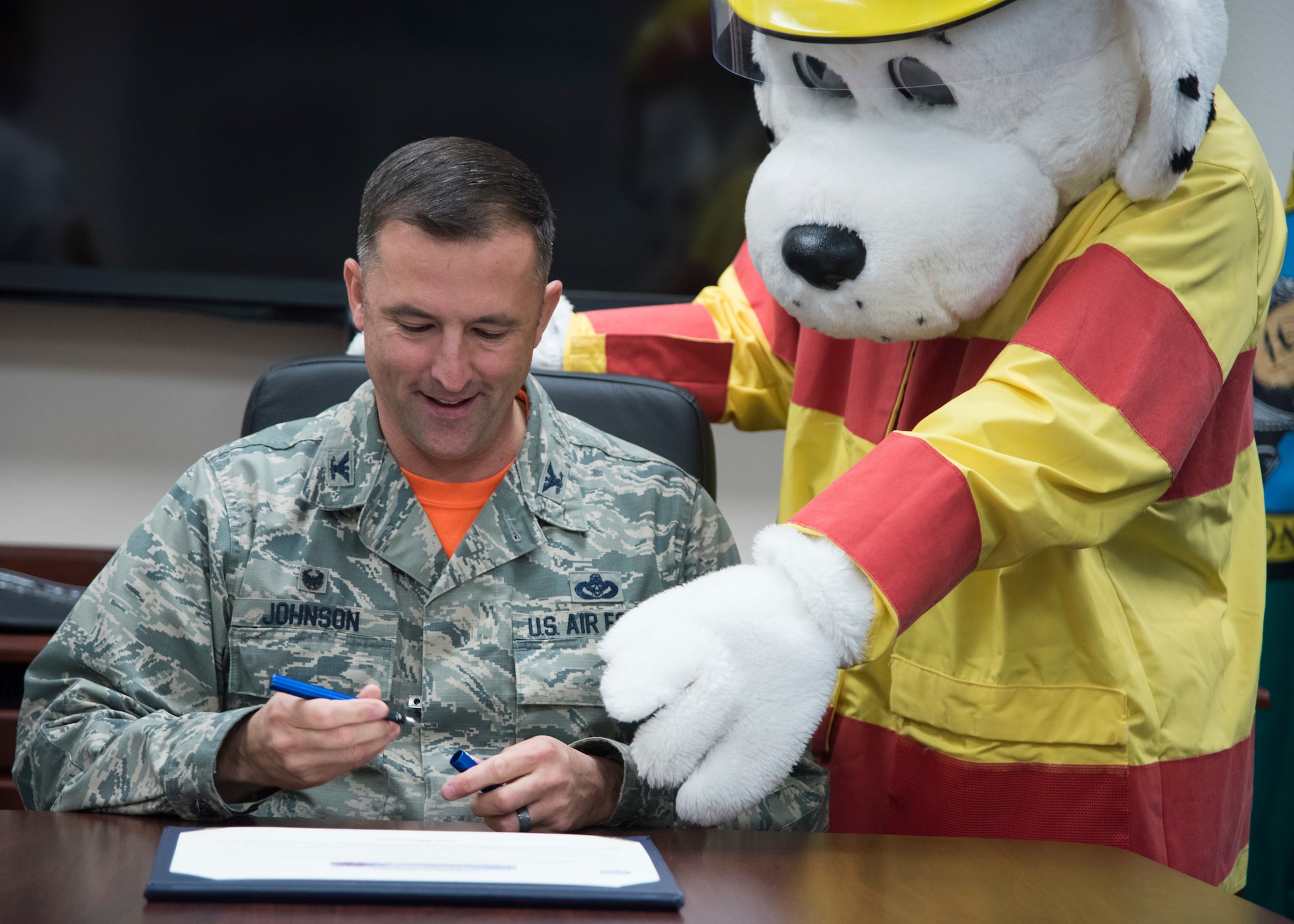 Col. Michael Johnson, 92nd Mission Support Group commander, is helped by Sparky the fire dog to sign a proclamation declaring the start of Fire Prevention Week at Fairchild Air Force Base, Washington, Oct. 5, 2018. The Team Fairchild firefighters raise awareness throughout the base via events, parades and carnival gatherings. (U.S. Air Force Photo/ Senior Airman Ryan Lackey)