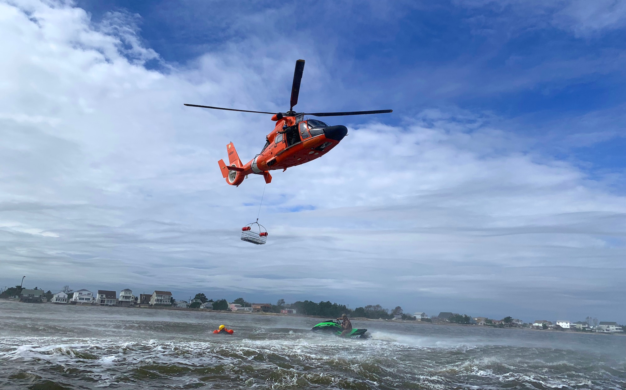 A Coast Guard HH-65 Dolphin helicopter lowers a rescue basket as a USCG rescue diver instructs an Air Force student how to safely ascend during water survival training Sept. 27, 2018, in the Atlantic Ocean off the coast of Bowers Beach, Del. This simulation provides Airmen with an opportunity to use the skills and tactics they learned in the classroom portion of the training.