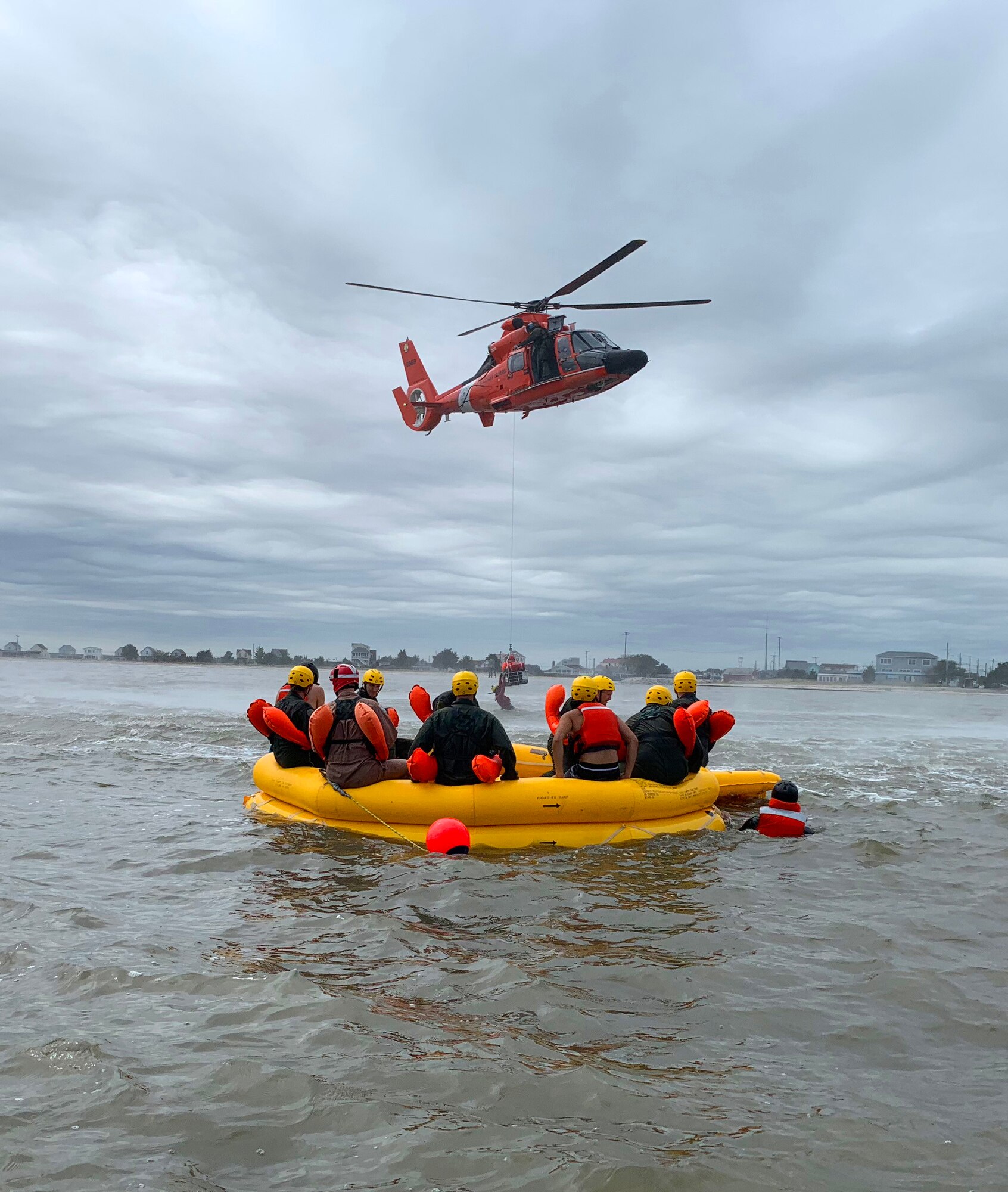 Airmen completing water survival training watch from a raft as a Coast Guard HH-65 Dolphin helicopter lifts a simulated survivor from the Atlantic Ocean Sept. 27, 2018, approximately 200 yards from the coast of Bowers Beach, Del. The Coast Guard rescue crew secured each Airman one by one and hoisted them into the aircraft to simulate a water rescue.