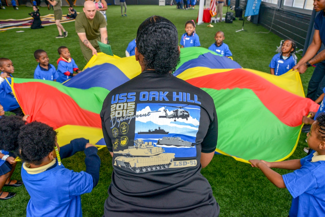 Sailors, Marines, and children grab the edges of a parachute in a circle.