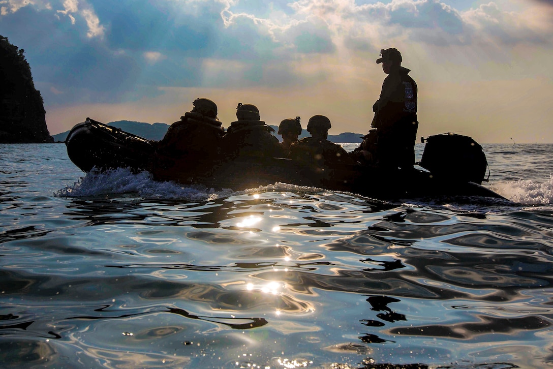 Marines ride in a rubber landing craft on calm waters today the shore.
